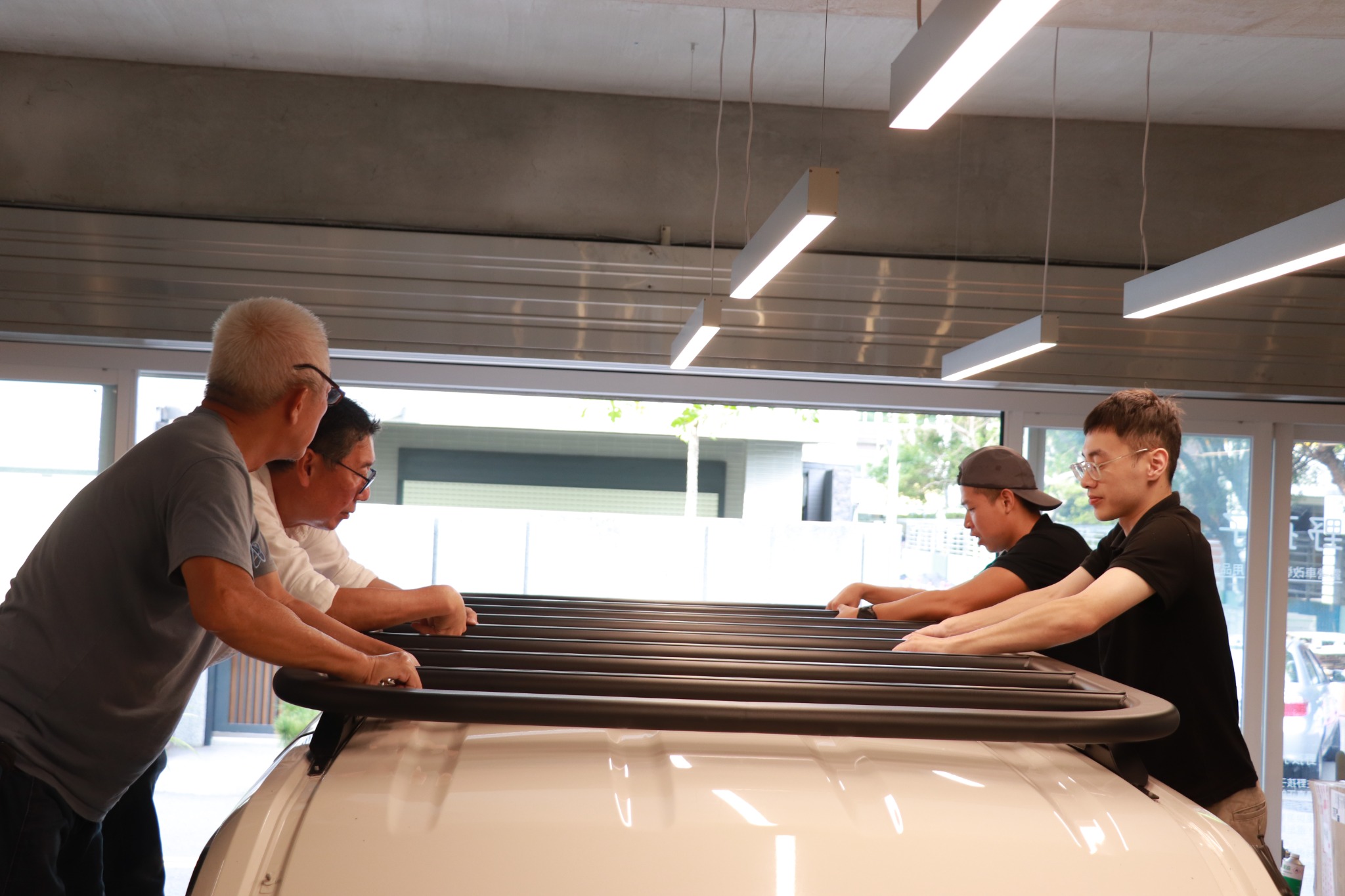 四人在白色車輛上方協作安裝金剛重力盤與車頂架，展示架體與橫桿